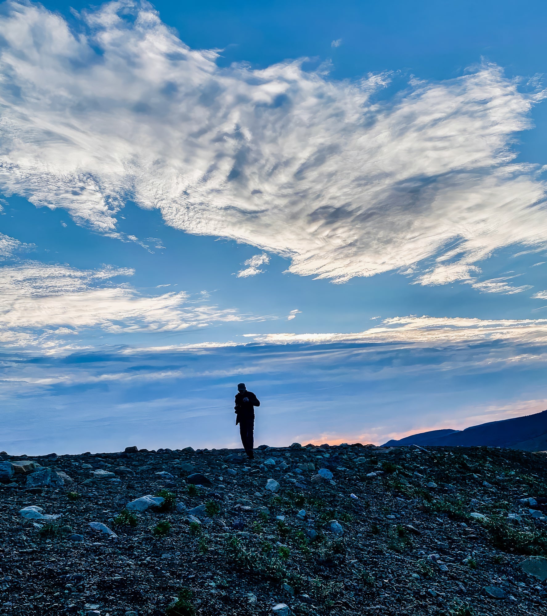 Person standing on a rocky landscape with a vast blue sky and scattered clouds