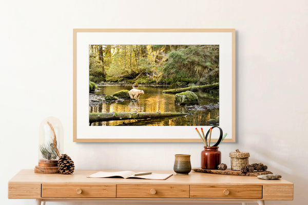 Framed nature print of a spirit bear standing in a forest scene hanging above a wooden desk with decorative items.