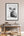 Framed black and white photo of a ram on a wall above a wooden bench with decor items.